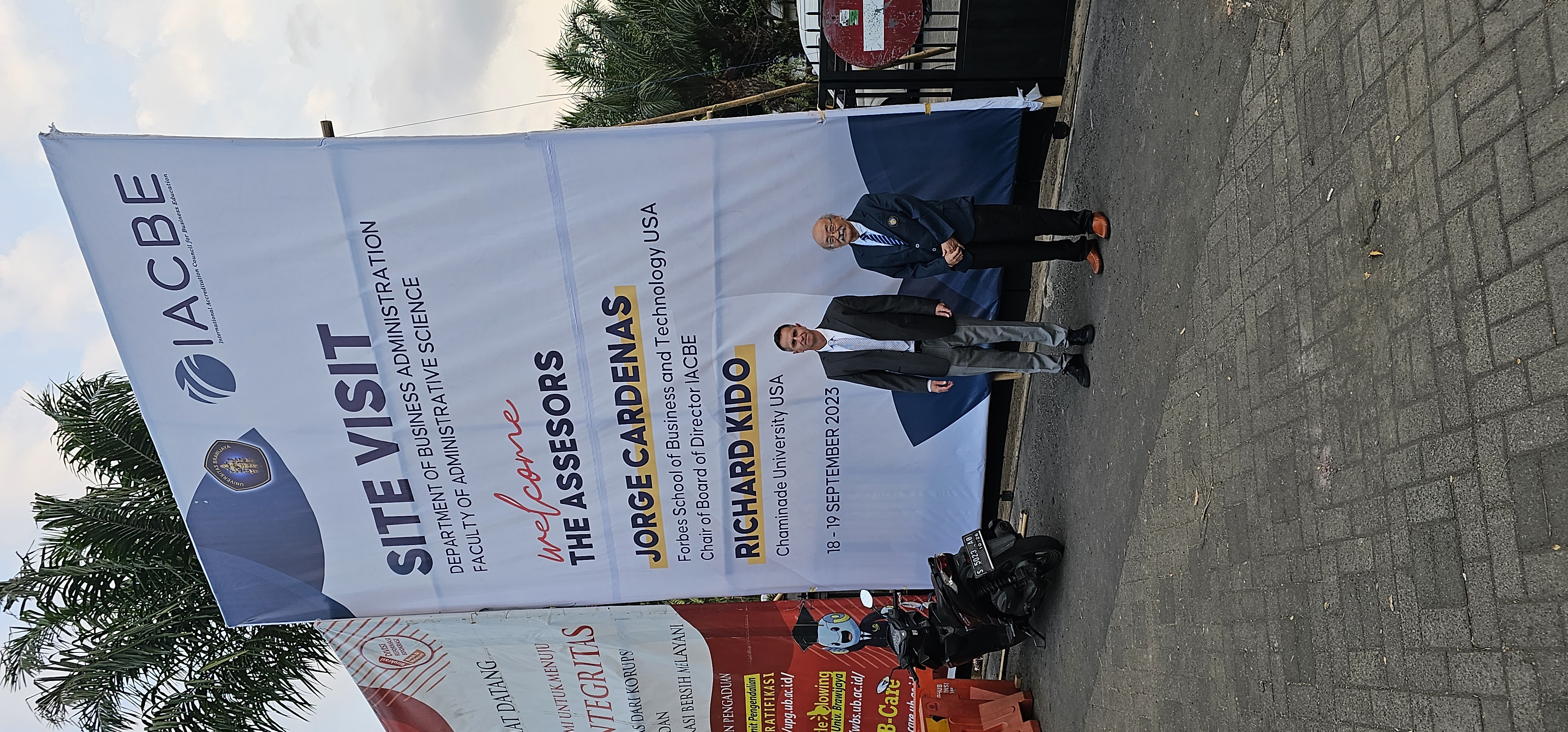 IACBE site visit reviewers Dr. Jorge A. Cardenas and Richard Kido in front of welcome banner at Brawijaya University Campus in Malang Indonesia.