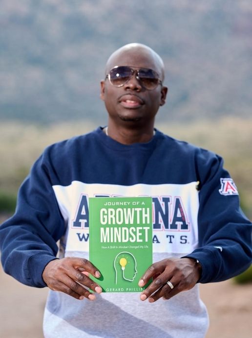 Gerard Phillips holding his first published book in a UA shirt