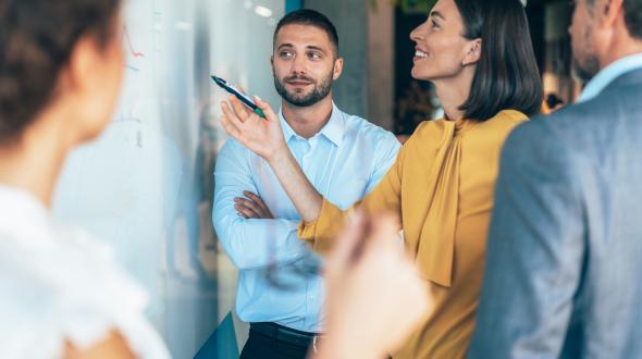 A woman writing on a whiteboard surrounded by her coworkers (Getty image)