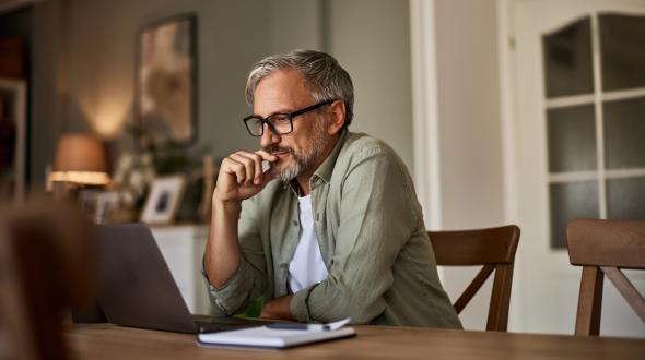 An older person sitting at a table looking at a laptop (Getty images)