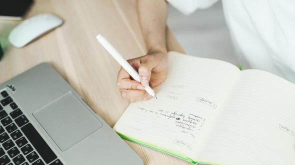 person's hand writing near a computer