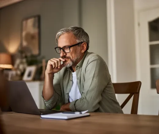 An older person sitting at a table looking at a laptop (Getty images)