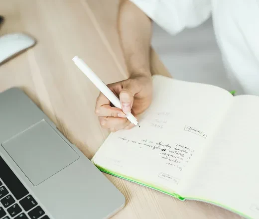 person's hand writing near a computer