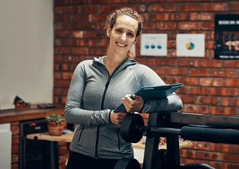 woman in workout gear with tablet by exercise equipment