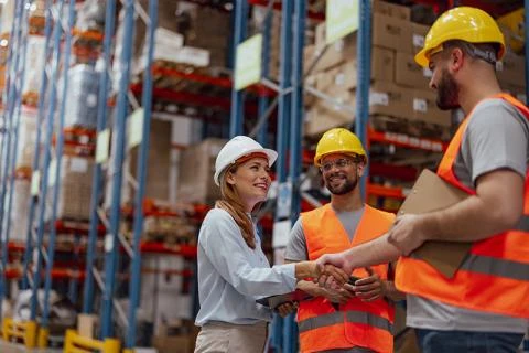 three people in hard hats in a warehouse shaking hands and smiling
