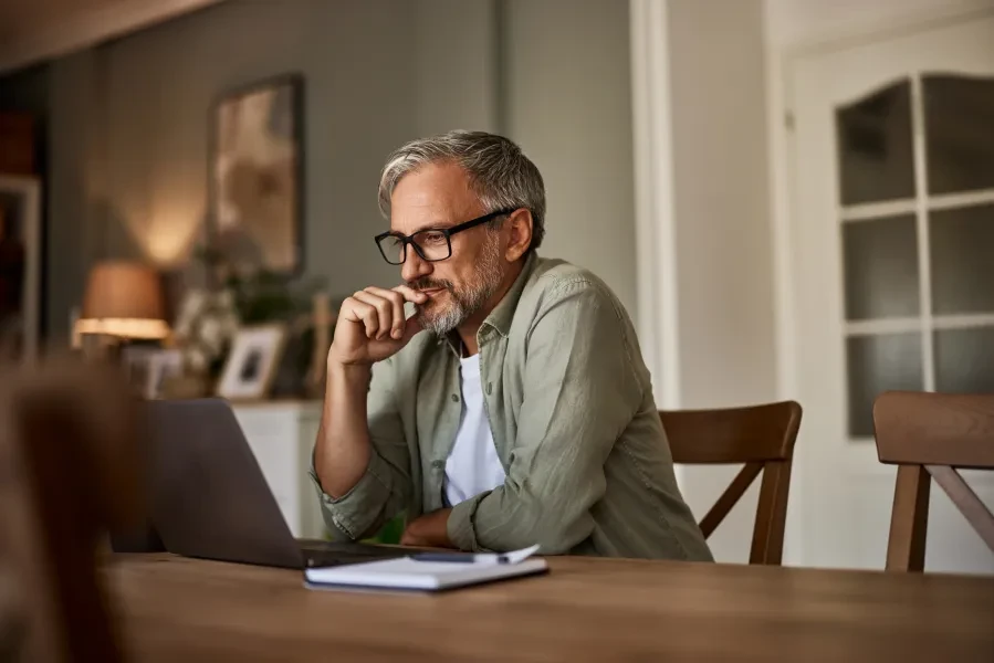An older person sitting at a table looking at a laptop (Getty images)