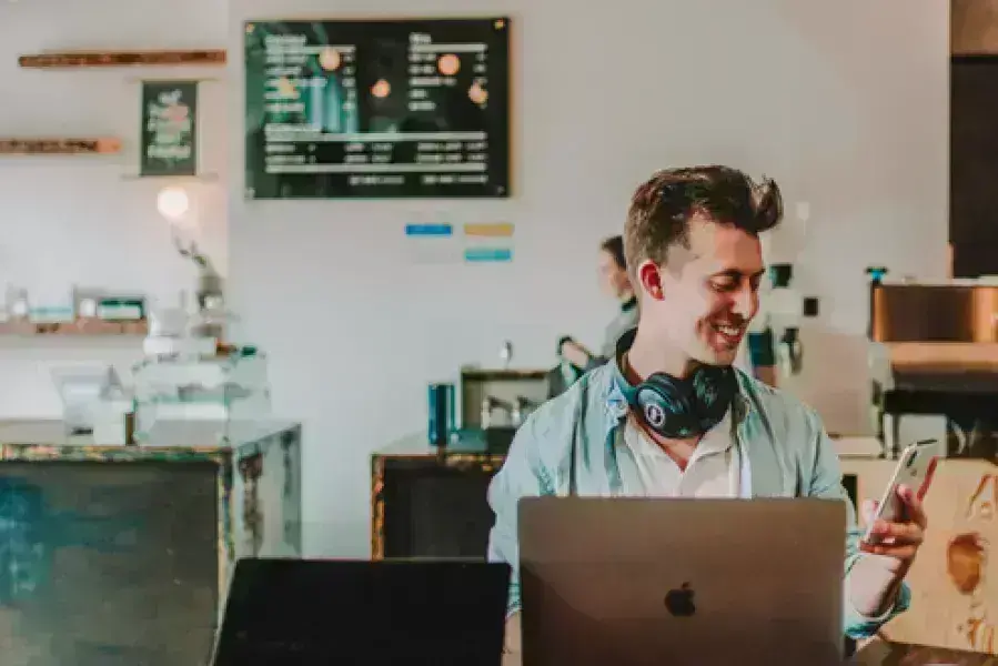 A person on their laptop smiling while looking at their cell phone