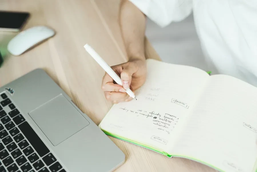 person's hand writing near a computer